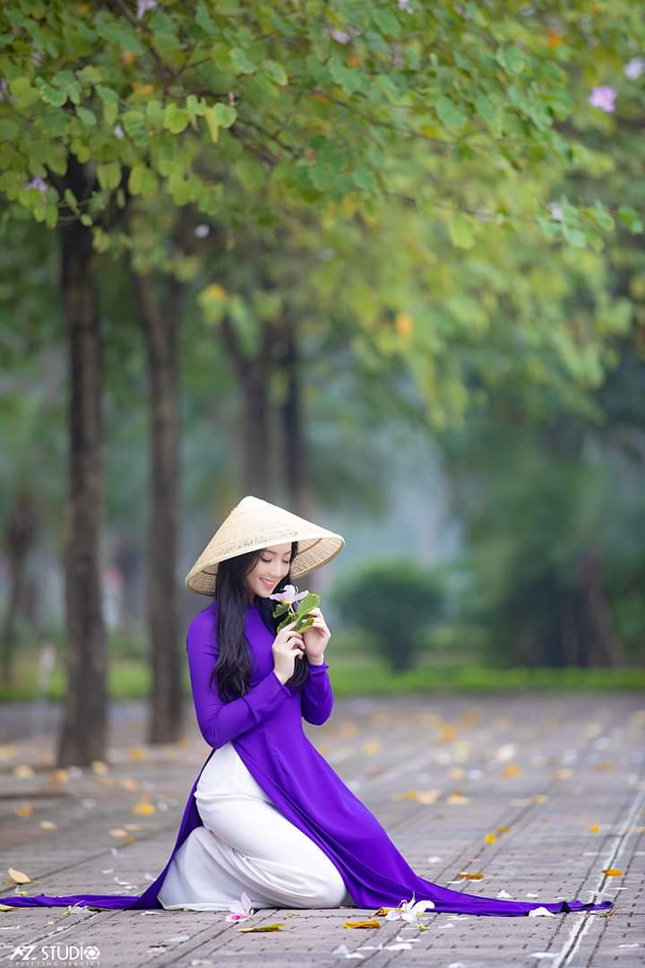 Tạo dáng ngồi trên gối với áo dài, tay cầm hoa, mắt nhìn vào hoa Tạo dáng ngồi trên gối với áo dài